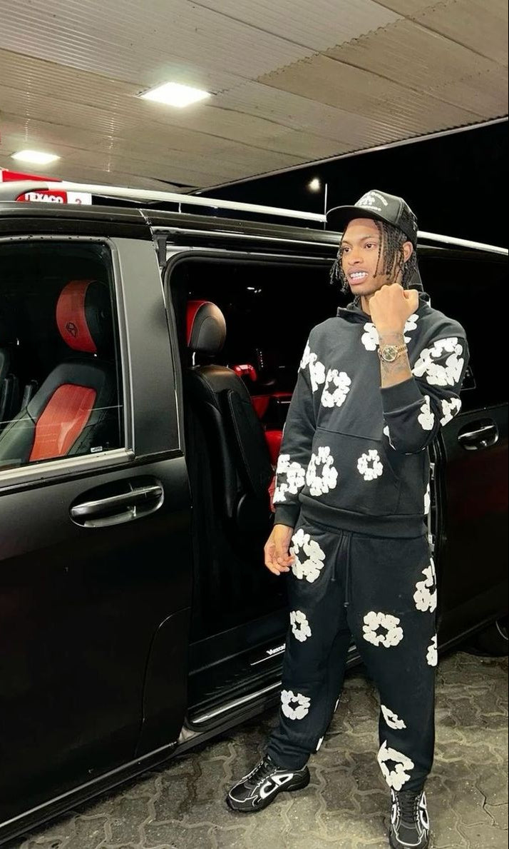 Person in a black and white floral outfit standing next to a black car with red interior.